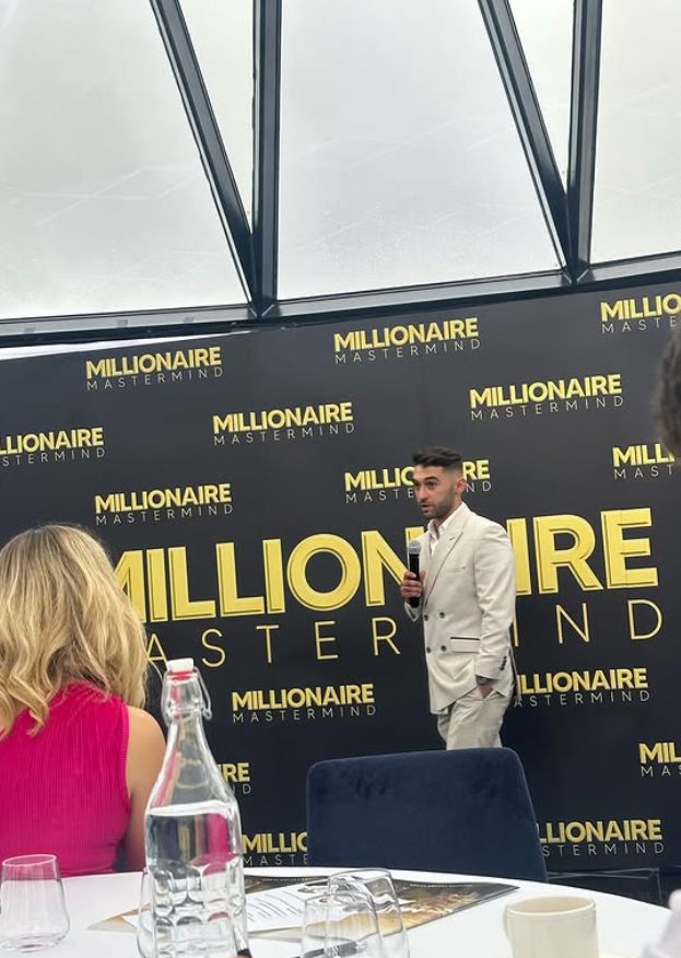 Tom speaking on stage with a microphone at a Millionaire Mastermind event